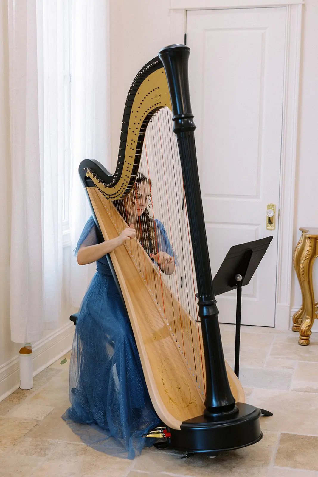 Korenna Hodge in elegant blue gown performing on harp indoors